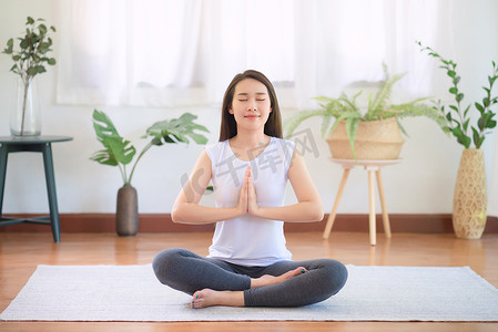 美丽的亚洲女性在家练习瑜伽时保持冷静和冥想，以追求健康的潮流生活方式