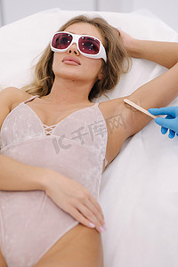 蓝色光芒的女美容师在美容工作室的女性腋窝上涂抹接触凝胶，进行激光脱毛。