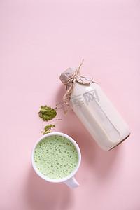 搅打的抹茶拿铁杯，一堆绿茶粉，一瓶健康有机有益健康的生纯素牛奶。