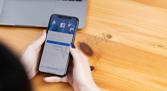 泰国清迈 - 2022年8月18日：女性手持iPhone X使用带有新登录屏幕的Facebook。Facebook是世界上最大的社交网络和最受欢迎的社交网站。
