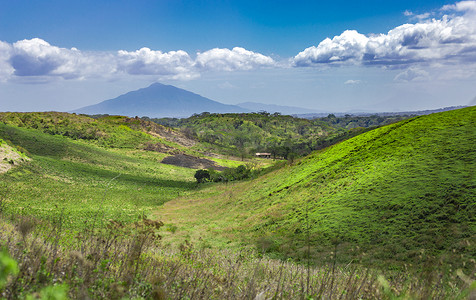 蓝天山谷摄影照片_山谷旁一座美丽的山丘，在阳光明媚的日子里，可以欣赏到带山丘和绿草的山谷