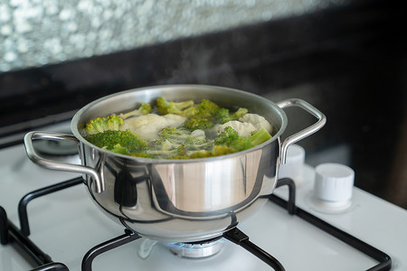 绿色新鲜西兰花在燃气白炉上的金属银锅中用水煮熟。
