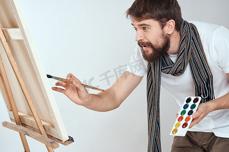 一位男艺术家在画架上画画，在业余爱好的创意浅色背景的手中画画