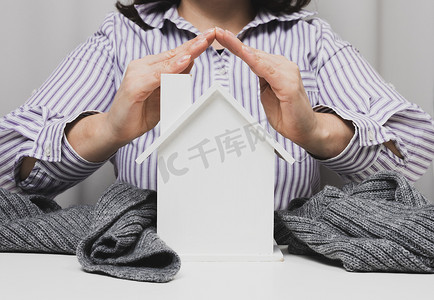 双手交叉摄影照片_女性双手交叉在白色背景的木制微型模型房子上。