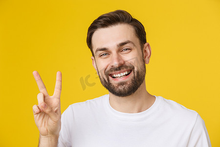 年轻英俊的男子穿着条纹 T 恤，在孤立的黄色背景上微笑着看着镜头，手指在做胜利的手势。