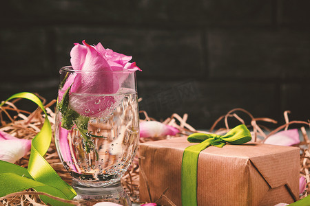 玻璃杯中的粉红玫瑰，桌上有水和装饰品