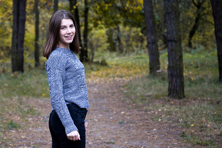 穿着灰色毛衣的可爱女孩在秋季森林的路上转了半圈。
