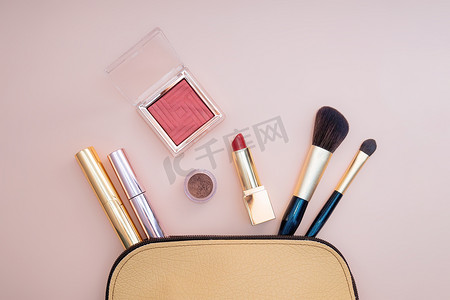从粉红色背景的米色化妆包中脱颖而出的化妆品的顶部视图