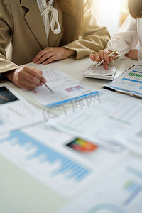 使用计算器分析图表公司财务预算报告和成本工作进度以及工作场所规划的业务伙伴关系同事的裁剪图像。