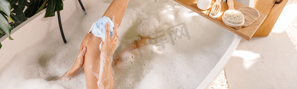 年轻女性在沐浴时使用海绵、在充满气泡的浴缸中放松的高视角