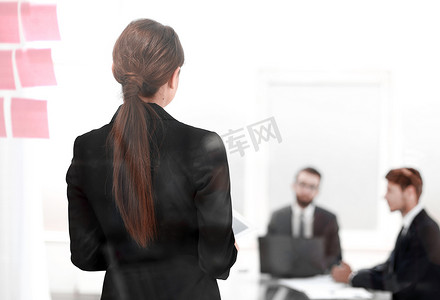 背面图。年轻的商界女强人站在办公室董事会前。