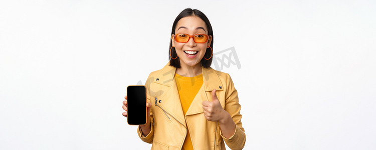 美丽的韩国女孩，戴墨镜的亚洲女性，展示智能手机应用界面，竖起大拇指，推荐手机应用，白色背景