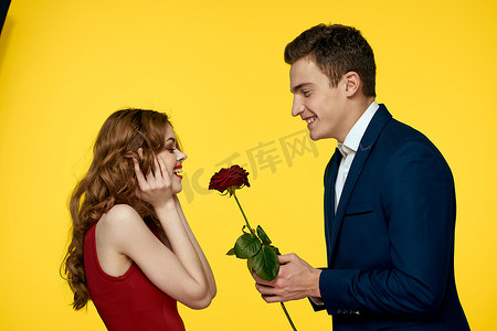 恋人男人和女人手里拿着一朵红玫瑰拥抱在黄色背景浪漫关系爱情家庭