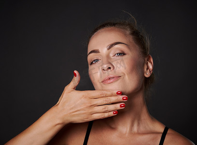 皮肤老化摄影照片_迷人的金发中年欧洲女性护理她的面部皮肤，在她的脸上涂抹平滑滋养抗衰老和抗皱保湿霜。