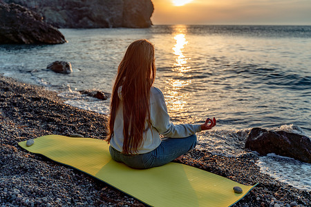 yoga摄影照片_长发飘逸的美丽女人在沙滩上练习瑜伽，半莲花姿势的 Yoga Ardha Padmasana。