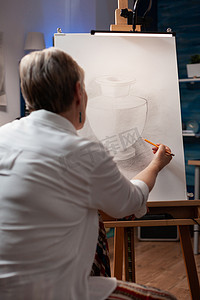 老年艺术家用锋利的铅笔在纸上素描花瓶模型上素描静物的肖像