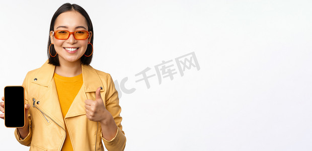 手机界面展示摄影照片_美丽的韩国女孩，戴墨镜的亚洲女性，展示智能手机应用界面，竖起大拇指，推荐手机应用，白色背景