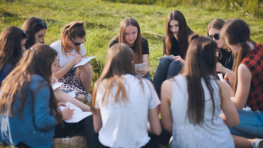 女人拿着笔记本摄影照片_一群女学生在草地上围坐成一圈，拿着笔记本集体作业。