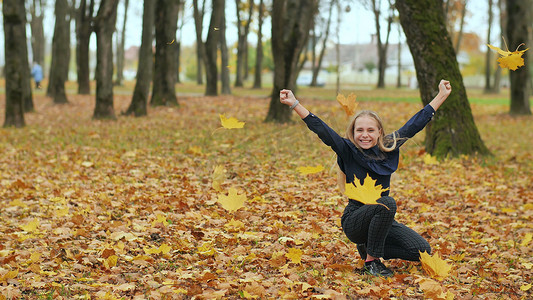 树叶飘动摄影照片_一个年轻的女学生在城市公园里扔秋叶。