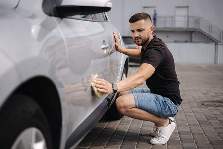 英俊的男人在自助洗车店的陈列室里用抹布擦拭汽车。