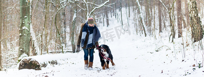 遛狗的女人摄影照片_冬天带着狗远足或散步的女人
