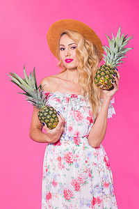 快乐的年轻女人拿着粉红色背景的菠萝。