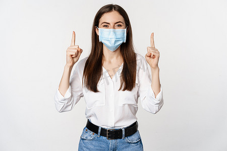 戴着冠状病毒医用口罩的企业女性肖像，手指向上，展示广告，白色背景