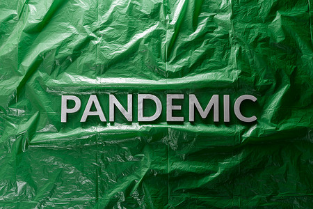 医务室背景摄影照片_“流行病”这个词在绿色皱巴巴的塑料薄膜背景上用银色字母铺成，中间为平躺组合物