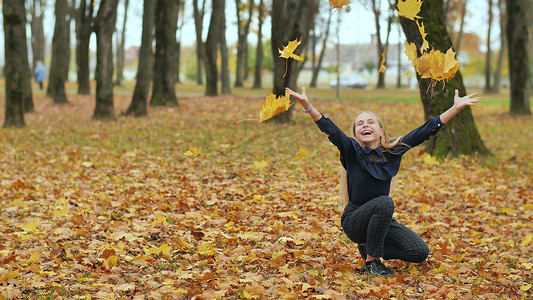 一个年轻的女学生在城市公园里扔秋叶。
