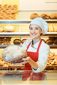 穿着围裙的女摄影照片_穿着围裙的女售货员在面包店里展示新鲜面包