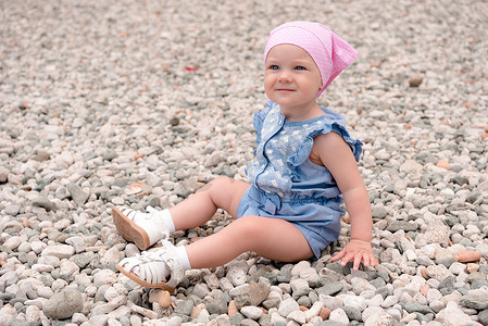 坐在沙滩上的小女孩，身上有穿着蓝色西装的海卵石