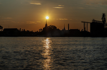 日出时阳光下，泰国寺庙剪影和湄南河沿岸工业工厂的美丽风景。