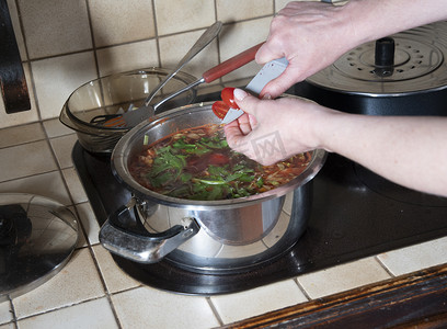 一个女人把樱桃番茄放在锅里，做罗宋汤的配料