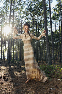 日落时分，一位身穿裙子的女士在森林针叶树和地面上的球果树中用手做手势