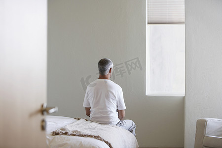 中年男子坐在卧室床边的后视图