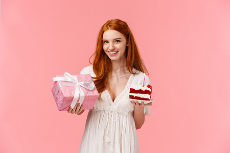 迷人的红发女友安排了很棒的生日派对，要求许个愿，吹灭蜡烛，拿着和平生日蛋糕和可爱的礼物，送礼物微笑，粉红色背景