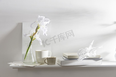 一个带白色虹膜的花瓶，不同尺寸的杯子，照片框，桌子上的盒子和相册。