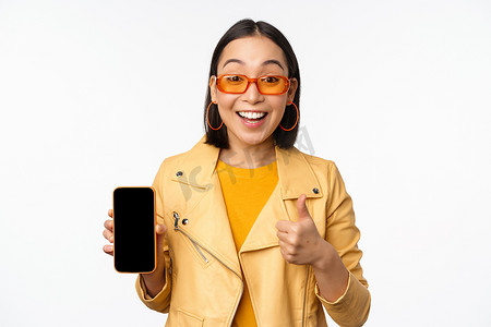 美丽的韩国女孩，戴墨镜的亚洲女性，展示智能手机应用界面，竖起大拇指，推荐手机应用，白色背景