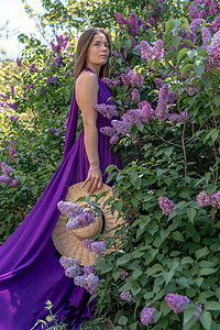 淡紫色花中的时装模特，穿着美丽长裙的年轻女子在风中挥舞，盛开的花园中的户外美女肖像