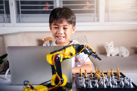 编程教育摄影照片_亚洲小男孩编程代码到笔记本电脑上的机器人机械臂下棋