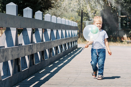 城市漫步摄影照片_一个孩子在城市的一个阳光明媚的夏日走过一座桥，带着一个热气球