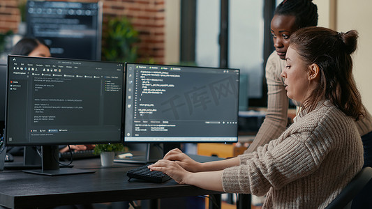 初级程序员在经验丰富的同事监督下编写算法，坐在有多个屏幕的办公桌前