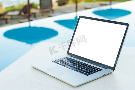 在阳光明媚的天气里，一台屏幕空白的笔记本电脑矗立在一个美丽的家庭花园的庭院里。