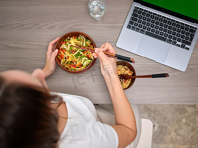 一个女人在电脑前用筷子吃饭的俯视图