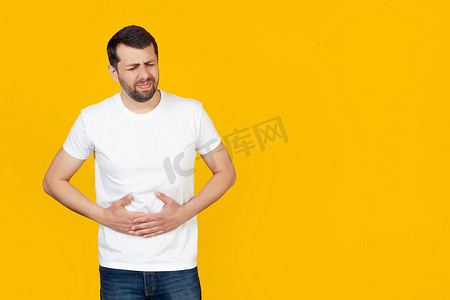 一名身穿白色T恤、留着胡须的年轻人，因消化不良，一只手放在肚子上，感觉不舒服。