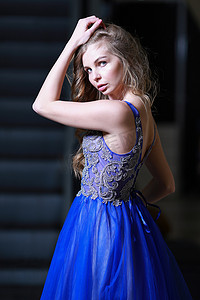 身着飘逸的蓝色晚礼服、背景是移动楼梯的金发美女