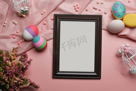 空相框与彩绘复活节彩蛋和粉红色背景上的春天的花朵。