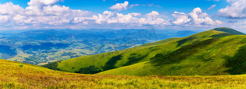 游动摄影照片_喀尔巴阡山脉明亮的山峰覆盖着绿草，白色蓬松的云彩在上面游动