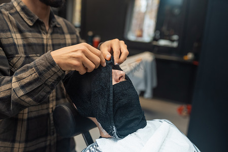 热毛巾摄影照片_理发师在理发店准备用热毛巾剃须的男人脸