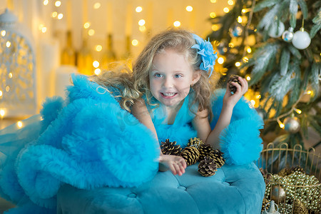 年轻漂亮的女孩穿着蓝色白色优雅的晚礼服，坐在圣诞树附近的地板上，在除夕夜送礼物。